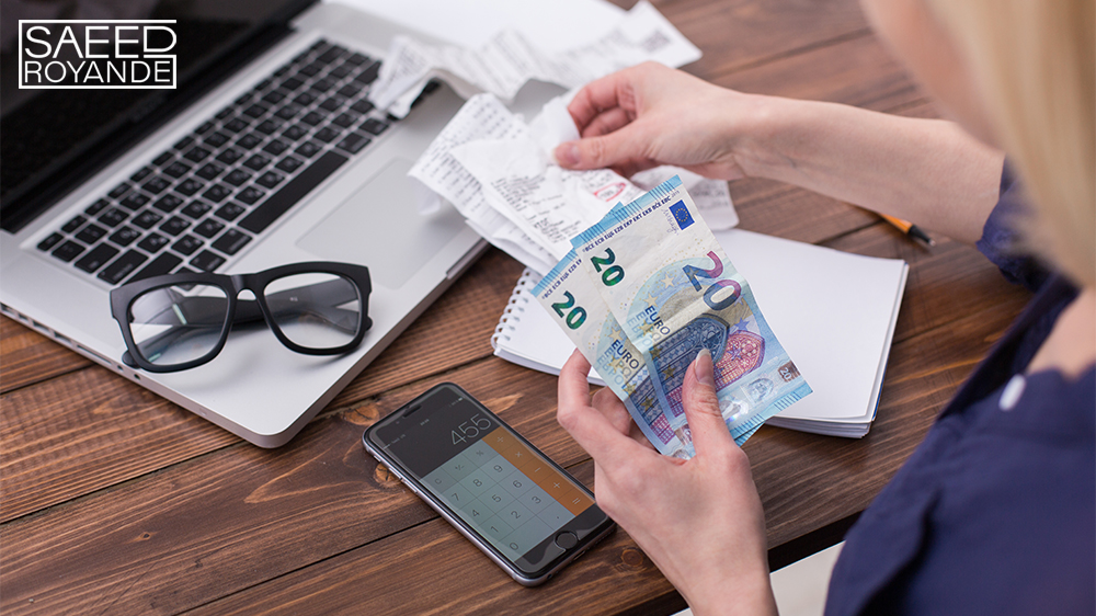 A young woman with a laptop holds money and bills